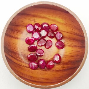 May include: A wooden bowl filled with 16 oval-shaped, faceted, ruby red gemstones.
