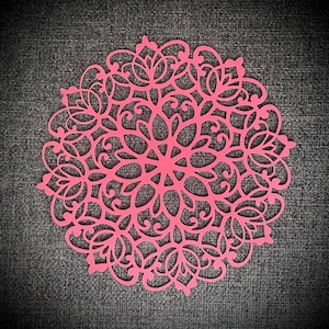 May include: Pink paper doily with a delicate floral design. The doily is circular and has an intricate pattern of flowers and leaves.