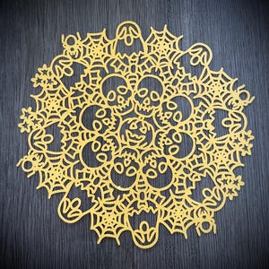 Puede incluir: Un encaje de papel amarillo con temática de Halloween. El encaje está decorado con un patrón repetitivo de calaveras, fantasmas, arañas y telarañas.