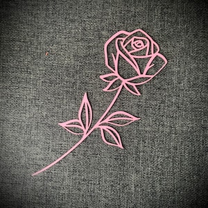 May include: A pink paper rose with a stem and leaves. The rose is cut out of paper and has a delicate, intricate design.