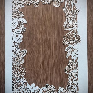 May include: White paper with a decorative border of butterflies and flowers cut out. The border is around a rectangular frame.
