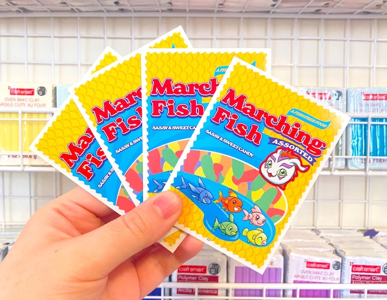Pu&ograve; includere: Una mano tiene una pila di quattro pacchetti gialli e blu di caramelle "Marching Fish". I pacchetti presentano un pesce dei cartoni animati con una coda arcobaleno e il testo "Sassy & Sweet Candy".