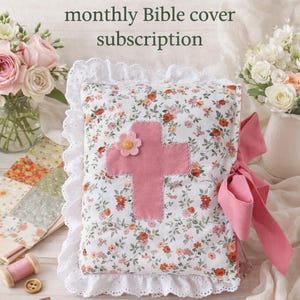 May include: A floral print Bible cover with a pink cross applique and a pink bow. The cover is surrounded by a white lace trim. The text "Pastures And Patchwork monthly Bible cover subscription" is at the top.