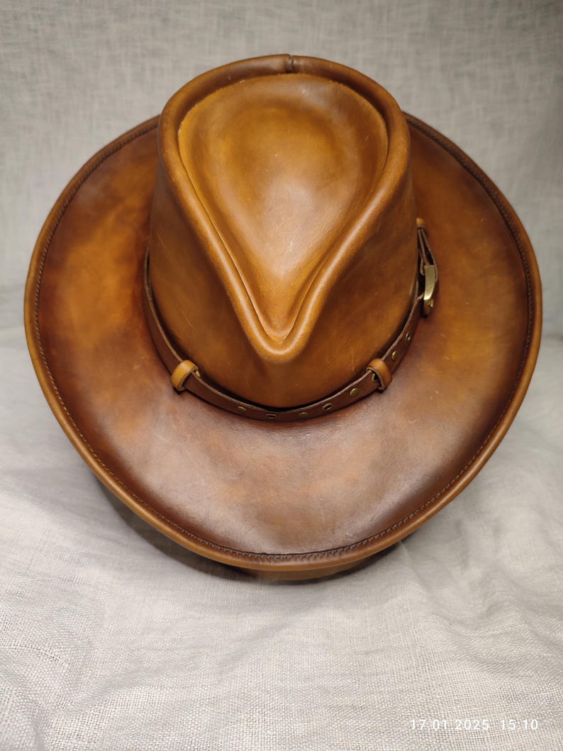 K&ouml;nnte beinhalten: Brauner Cowboyhut aus Leder mit breiter Krempe und spitz zulaufender Krone. Der Hut hat ein Lederband mit einer Messingschnalle. Ein klassischer Westernhut.