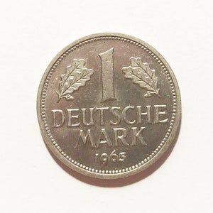 Può includere: Una moneta tedesca da 1 Deutsche Mark in argento del 1965. La moneta presenta un disegno a foglia di quercia su entrambi i lati del numero "1" e le parole "Deutsche Mark" sotto.