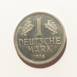 May include: A silver German 1 Deutsche Mark coin from 1965. The coin features an oak leaf on each side of the number "1" and the words "Deutsche Mark" below.