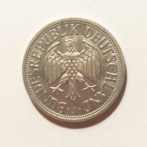 May include: A silver German coin with the words "Bundesrepublik Deutschland" around the edge and a stylized eagle in the center.