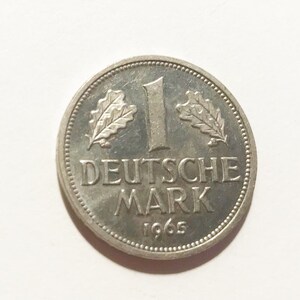 May include: A silver German 1 Deutsche Mark coin from 1965. The coin features an oak leaf on each side of the number "1" and the words "Deutsche Mark".