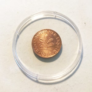 Könnte beinhalten: Eine kupferfarbene Münze mit der Aufschrift "BANK DEUTSCHER LANDES 1949" und einem Eichenblatt-Design.