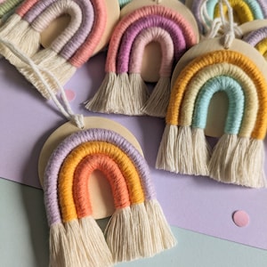 Könnte beinhalten: Ein Set aus bunten regenbogenförmigen Ornamenten mit Fransen, die jeweils aus Garn bestehen, das um einen Holzkreis gewickelt ist. Die Regenbögen sind in den Farben Rosa, Lila, Gelb, Orange und Blau gehalten.