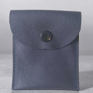 May include: A square-shaped navy blue leather pouch featuring a textured surface and a single centered black snap button closure on the front flap. The pouch has visible stitching along the side edges and a smooth, consistent dark blue color.