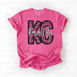 May include: Pink t-shirt with a black and white leopard print design that says "KC Kansas City" in white text.
