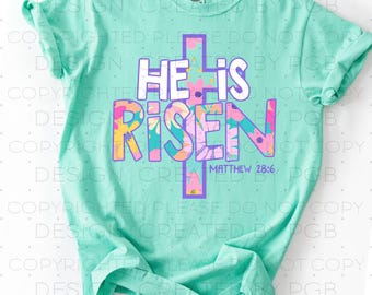 May include: A turquoise t-shirt with a floral design and the words "He is Risen" with a purple cross behind the text. The text "Matthew 28:6" is below the cross.