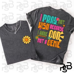 May include: A charcoal gray t-shirt featuring a small yellow flower on the front left chest and a large back graphic with the text I PRAY NOT WISH BECAUSE I HAVE GOD NOT A GENIE in colorful retro-style lettering with small flower and star accents.