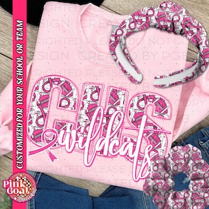 May include: A pale pink sweatshirt featuring the text "OHS Wildcats" in white script and block letters. The letters are filled with a pattern of pink ribbons and footballs. A matching headband and a patch are also visible.