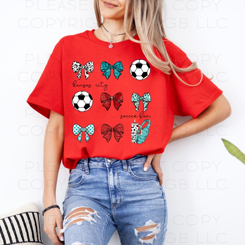 May include: A red t-shirt featuring a soccer theme. The shirt displays soccer balls, bows, and the text "Kansas City" and "soccer fan". The bows have various patterns and colors, including black and white, teal, and red.