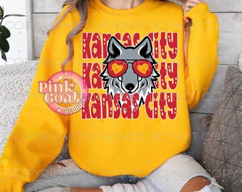 Könnte beinhalten: Gelber Pullover mit einem roten Aufdruck eines Wolfes, der eine Herzform-Sonnenbrille trägt, und dem Text "Kansas City", der dreimal wiederholt wird. Der Text ist von roten Herzen umgeben.