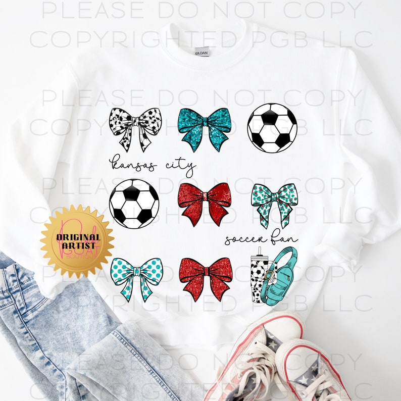 May include: White sweatshirt featuring soccer-themed graphics. The design includes soccer balls, bows in various patterns and colors, and the text "Kansas City" and "soccer fan". The sweatshirt also has a "Original Artist" seal.