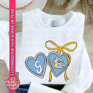 May include: White sweatshirt featuring a heart-shaped pendant with a bulldog graphic and the letter "G". The pendant is light blue with a yellow ribbon. Text on the side reads "CUSTOMIZED FOR YOUR SCHOOL OR TEAM".