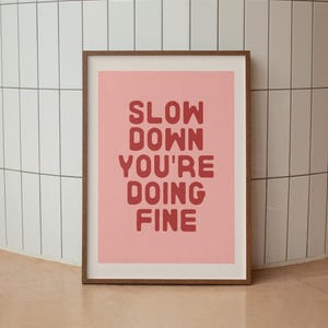 May include: A pink framed print with the text "SLOW DOWN YOU'RE DOING FINE" in red.