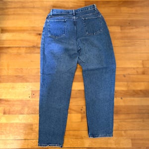 May include: A pair of blue denim jeans, viewed from the back, with two back pockets and a classic straight leg design. The jeans are made of a medium-wash denim fabric and feature a button and zipper closure.