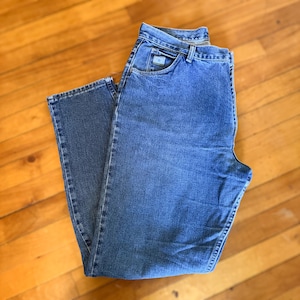 May include: A pair of blue denim jeans with a classic five-pocket design. The jeans have a straight leg cut and a button and zipper closure. The jeans are made of a medium-wash denim fabric and feature a small logo on the front pocket.