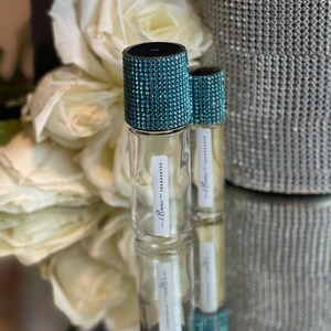 K&ouml;nnte beinhalten: Zwei klare Glasflaschen mit t&uuml;rkisfarbenen Strasssteinen. Die Flaschen sind mit "Illum - Fragrance" beschriftet.