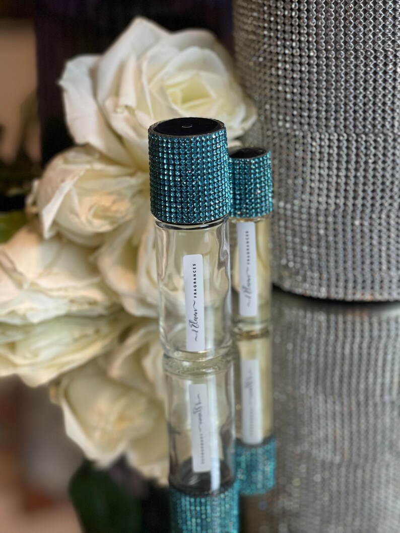 K&ouml;nnte beinhalten: Zwei klare Glasflaschen mit t&uuml;rkisfarbenen Strasssteinen. Die Flaschen sind mit "Illum - Fragrance" beschriftet.