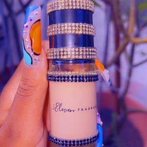 K&ouml;nnte beinhalten: Eine kleine, durchsichtige Glasflasche mit einem schwarzen und goldenen Verschluss. Die Flasche ist mit Strasssteinen verziert und tr&auml;gt den Schriftzug "2 Eleven Fragrances" auf dem Etikett.