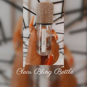 K&ouml;nnte beinhalten: Eine klare Glasflasche mit einem verzierten Verschluss. Die Flasche ist mit "Elara Fragrances" beschriftet.