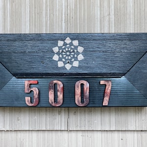 May include: A black wooden mailbox with a white geometric design and the number 5007 in red.