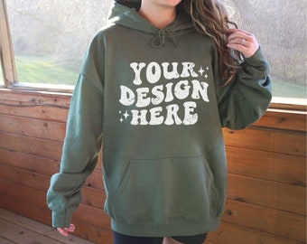 May include: A green hooded sweatshirt with the text "YOUR DESIGN HERE" in white, distressed lettering. The sweatshirt has a pouch pocket and is being worn by a person.