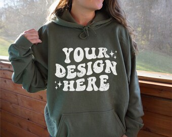 Puede incluir: Una sudadera con capucha verde con el texto "YOUR DESIGN HERE" en blanco con una fuente retro desgastada. El texto está rodeado de pequeñas estrellas blancas.