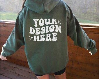 Puede incluir: Una sudadera con capucha verde oscuro con el texto "YOUR DESIGN HERE" en blanco en la parte posterior. El texto tiene un aspecto desgastado y vintage.