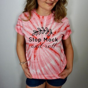 Può includere: Una maglietta tie-dye rosa e bianca con una grafica nera che dice "Stop Mock and roll" con un piccolo disegno di ramo sopra il testo.