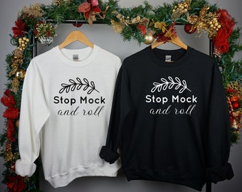 May include: Two sweatshirts, one white and one black, with the text "Stop Mock and roll" and a small leaf design. The sweatshirts are hanging on a rack with a Christmas garland behind them.