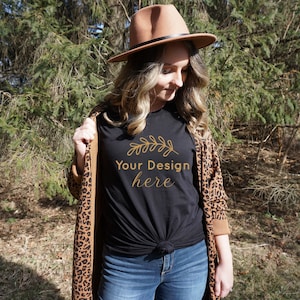 May include: A black t-shirt featuring a gold leaf design and the text "Your Design here". The shirt is being worn by a person wearing a brown hat and a leopard print cardigan.