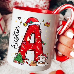 May include: White ceramic mug with a red interior and handle, featuring a large red letter "A" decorated with Christmas-themed illustrations. The name "Austin" is written on the side. A candy cane is placed inside the mug.