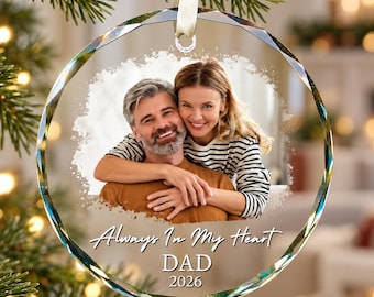 May include: A round, faceted glass Christmas ornament featuring a printed photograph of a smiling couple embracing. The text "Always In My Heart", "DAD", and "2026" is printed in white below the image. A cream ribbon is attached for hanging.