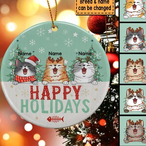 May include: A round, green and white Christmas ornament with three cats wearing Santa hats and reindeer antlers. The cats are in front of Christmas trees and the ornament says "Happy Holidays".