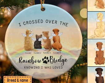 May include: A round, white ceramic ornament with a colorful rainbow and the text "I crossed over the Rainbow Bridge knowing I was loved". Four dogs with angel wings are sitting on a cloud above the rainbow. The ornament is personalized with the names "NAME", "NAME2", "NAME3", and "NAME4".