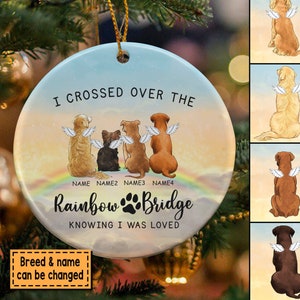 May include: A round, white ceramic ornament with a colorful rainbow and the text "I crossed over the Rainbow Bridge knowing I was loved". Four dogs with angel wings are sitting on a cloud above the rainbow. The ornament is personalized with the names "NAME", "NAME2", "NAME3", and "NAME4".