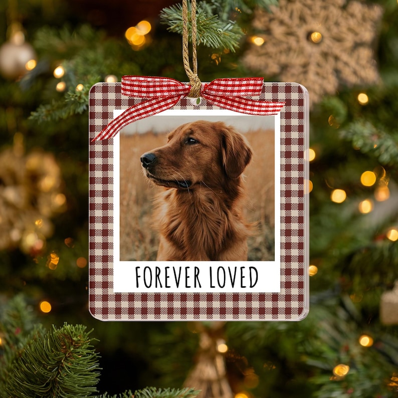 May include: A square hanging ornament featuring a brown and white gingham border and a central photograph of a golden-colored dog. The ornament includes a white bottom section with the black text FOREVER LOVED and a red and white gingham ribbon bow.