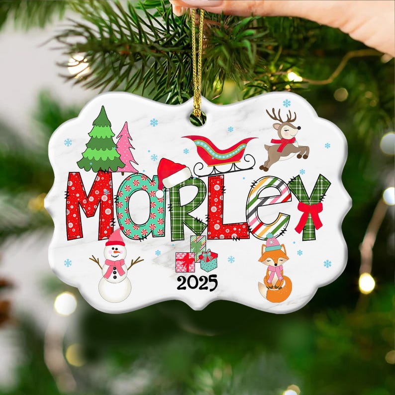 May include: A white ceramic Christmas ornament with the name "MORLEY" in colorful letters. The ornament features festive illustrations of a Christmas tree, snowman, reindeer, fox, and gifts. The year "2025" is also displayed.