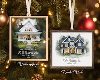 May include: Two square hanging ornaments featuring watercolor-style house illustrations. The left ornament has a light wood frame, a white house, and text reading OUR 1ST CHRISTMAS AT 50 S GRAND AVE LUCAS & KAREN 2026. The right has a dark wood frame, a blue house, and text reading FIRST CHRISTMAS AT 1001 JERSEY ST. THE WILSONS 2026.