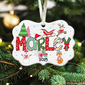May include: A white ceramic Christmas ornament with a scalloped edge, featuring the name "MORLEY" in festive lettering. The design includes a Christmas tree, snowman, reindeer, fox, and the year 2025. A white ribbon is attached for hanging.