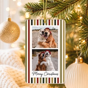 May include: A rectangular Christmas ornament featuring a vertical striped border in red, dark green, and cream. The center displays two stacked photos of two dogs wearing red hats, with the text Merry Christmas written in black script below.