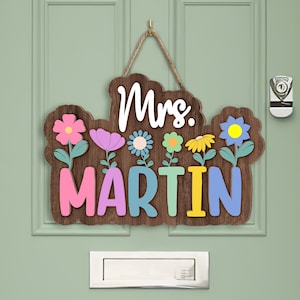 May include: Wooden door sign with the text "Mrs. MARTIN" in colorful letters. The sign is decorated with flowers in pink, blue, yellow, and green.