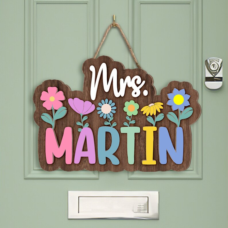 May include: Wooden door sign with the text "Mrs. MARTIN" in colorful letters. The sign is decorated with flowers in pink, blue, yellow, and green.