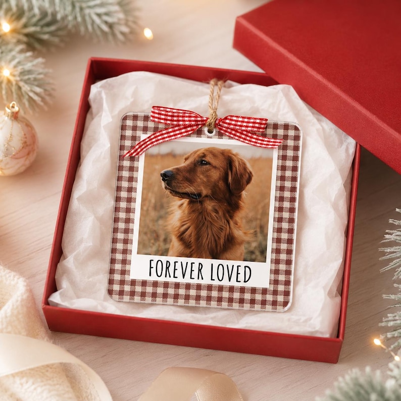 May include: A square acrylic ornament featuring a brown and white gingham border and a photograph of a golden-colored dog. The ornament includes a red and white checkered ribbon at the top and the text FOREVER LOVED printed in black.